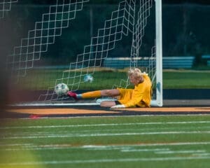 Goalkeeper in yellow gear dives for a soccer ball in the net, capturing an intense moment during the match.