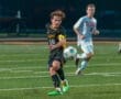 High school soccer match: player in black dribbles the ball while an opposing player in white pursues.