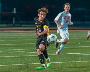 High school soccer match: player in black dribbles the ball while an opposing player in white pursues.