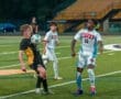 High school soccer players compete for possession of the ball under lights on a turf field during a match.