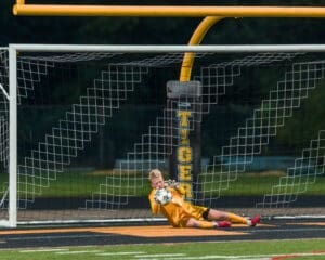 Young goalkeeper in yellow jersey making a save during a soccer game, with a colorful ball in the net.