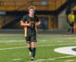 High school soccer player wearing a black and yellow Tigers uniform, running on the field during a game at night.