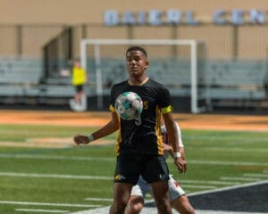 A soccer player in a black and yellow uniform skillfully controls the ball on the field during a match.