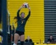 Volleyball player preparing to serve, showcasing athleticism against a vibrant yellow background in a gym setting.