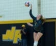 Volleyball player serving during a match, focused and poised, with a photographer capturing the action in the background.