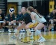 Volleyball players strategizing during a game, focusing on a high-flying ball in a competitive gym setting.