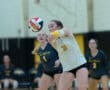 Volleyball player in action, setting up for a serve with teammates in the background during a competitive match.
