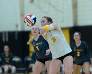 Volleyball player in action, setting up for a serve with teammates in the background during a competitive match.