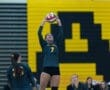 Volleyball player wearing jersey number 7 sets the ball while teammates watch during a match against a vibrant backdrop.