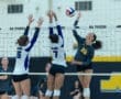 High school volleyball match with players jumping at the net to block a spike during an intense game moment.