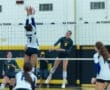 Two volleyball players leap at the net in an intense match, showcasing athleticism and teamwork in a gym setting.