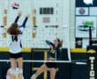 Two female volleyball players in action during a game, one attempting a block while the other strikes the ball.