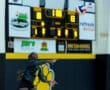 Volleyball player serving during a match, with the scoreboard showing a close game at 18-13.