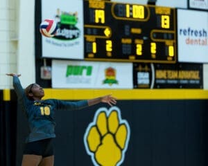 Player serves in a volleyball match, with the score at 19-13 and one minute left on the clock.