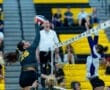 A volleyball player in action jumps to spike the ball over the net as a defender attempts to block. Energetic game moment.