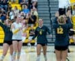 High school volleyball team celebrating a point with excitement during a match in a gym filled with fans.