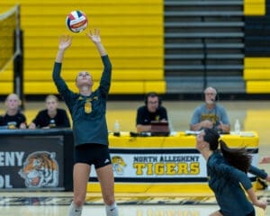 Volleyball player sets the ball in action during a game at North Allegheny High School, with teammates and announcers visible.