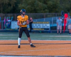 High school football player in yellow jersey, preparing for the game on the field with teammates in the background.