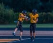 Two excited football players in yellow and black uniforms celebrate on the field, showcasing teamwork and sportsmanship.