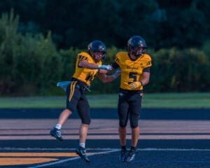 Two excited football players in yellow and black uniforms celebrate on the field, showcasing teamwork and sportsmanship.