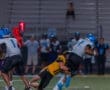 Football players in action during a night game, with a defender tackling the ball carrier on the field.