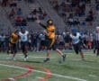 Quarterback in yellow jersey throws a football while being pursued by defenders in a night football game.