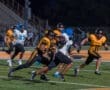 High school football players compete under stadium lights, with one player evading tackles during an intense game.