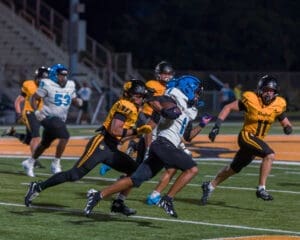 High school football players compete under stadium lights, with one player evading tackles during an intense game.