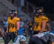 Two football players in yellow uniforms on the field, preparing for the next play during a night game.