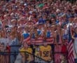 High-energy crowd at a night sports event, showcasing team spirit with patriotic attire and excited expressions.