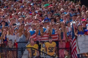 High-energy crowd at a night sports event, showcasing team spirit with patriotic attire and excited expressions.