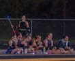Drill team members sitting on the sidelines during a night performance, enjoying snacks and preparing for their routine.