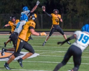 Quarterback wearing number 4 throws a pass while evading defenders during a night football game on the field.