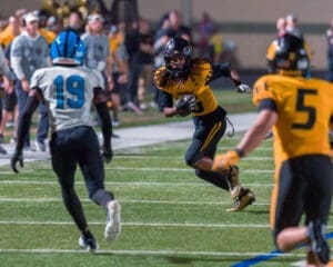 Football player in yellow jersey dodges opponent in blue during night game on the field, showcasing athleticism and competition.