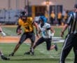 High school football game action with a quarterback in yellow avoiding a tackle from a defender in white.
