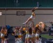 Cheerleader flying through the air as teammates catch her during a night game performance, showcasing teamwork and athleticism.
