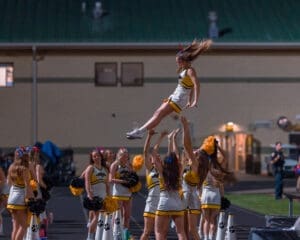 Cheerleader flying through the air as teammates catch her during a night game performance, showcasing teamwork and athleticism.