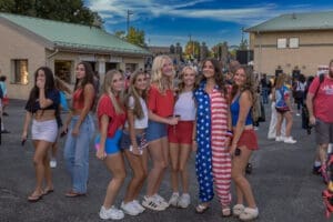 Group of friends dressed in patriotic outfits, smiling together at an outdoor event with a festive atmosphere.