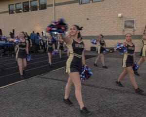 Cheerleaders in black and gold outfits perform with pom-poms at a school event, showcasing team spirit.