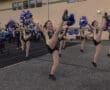 Cheerleaders performing energetic kicks while holding pom-poms at a sports event, showcasing teamwork and school spirit.