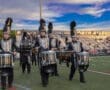Marching band members in uniforms play drums on the field during a performance at North Allegheny High School.