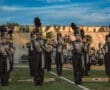Marching band members perform on field, showcasing instruments and uniforms at North Allegheny football stadium.
