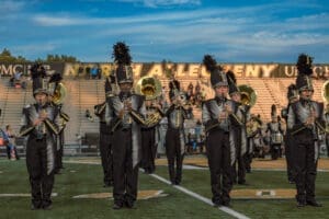 Marching band members perform on field, showcasing instruments and uniforms at North Allegheny football stadium.