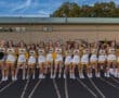 Cheerleaders in yellow and black uniforms smile and pose on the track at a sports event, showcasing team spirit and camaraderie.