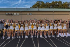 Cheerleaders in yellow and black uniforms smile and pose on the track at a sports event, showcasing team spirit and camaraderie.