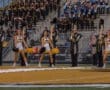 Cheerleaders and marching band performing at a high school football game, showcasing school spirit and teamwork.
