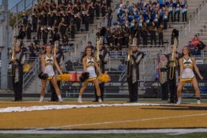 Cheerleaders and marching band performing at a high school football game, showcasing school spirit and teamwork.