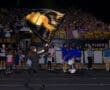 Cheerleader waving a black flag at a nighttime sports event, with an excited crowd in the background.