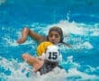 Two female water polo players compete in a match, focused on the ball amidst splashing water.