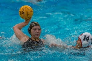 Water polo action shot: a player prepares to throw a water polo ball while another player defends nearby.